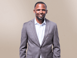 Smiling man in a brown suit and white shirt against a neutral background